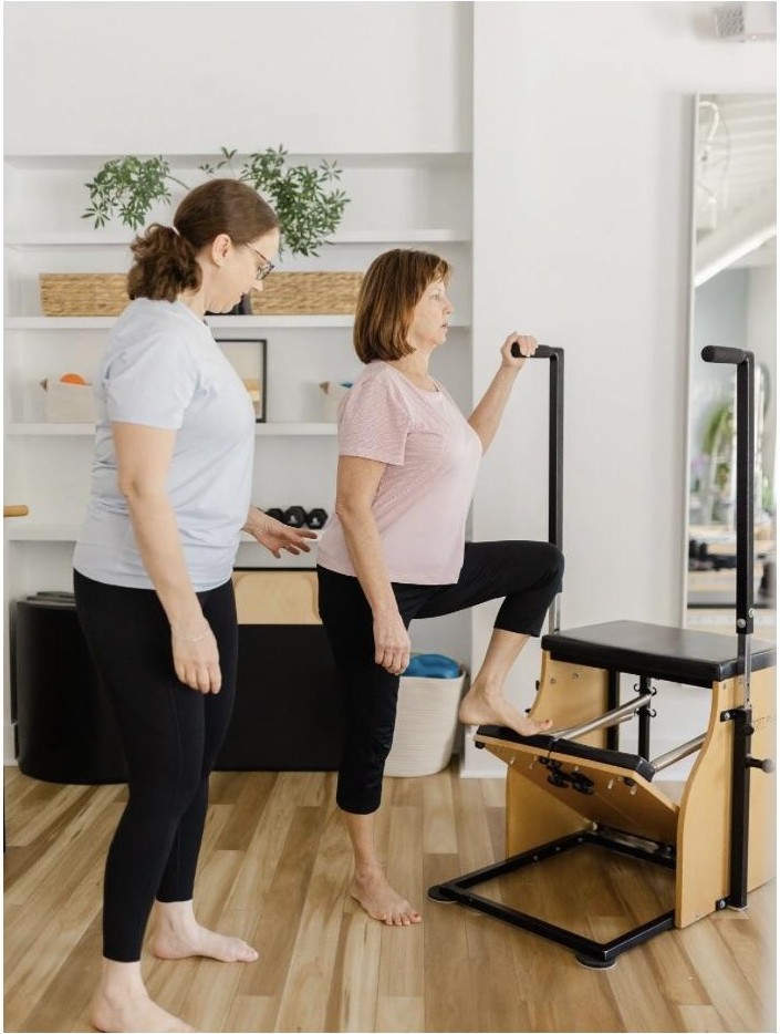 Anne working one-on-one with a client, guiding them through a Pilates exercise on studio equipment during an in-home therapy session.